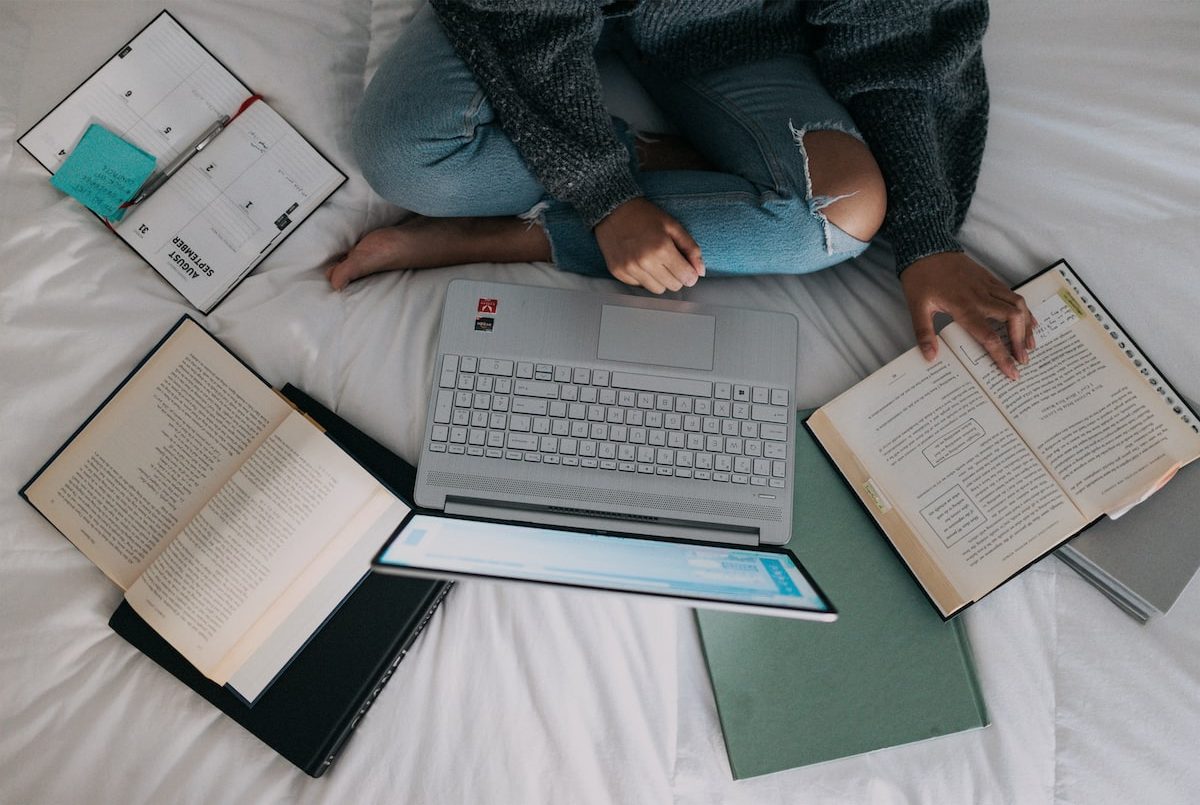 woman in blue long sleeve shirt and blue denim jeans sitting on bed using laptop